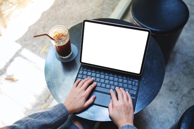 Draufsicht-Mockup-Bild einer Frau, die Tablett-Tastatur mit leerem weißem Desktop-Bildschirm als Computer-PC mit Kaffeetasse auf dem Tisch verwendet und tippt