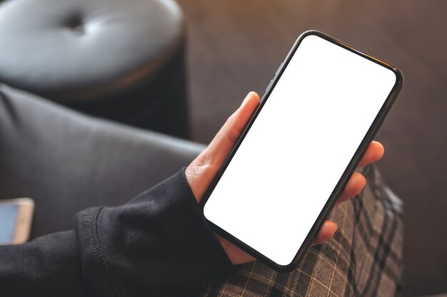 Draufsicht-Modellbild der Hände, die schwarzes Mobiltelefon mit leerem weißen Bildschirm im Café halten