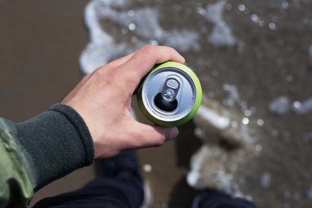 Draufsicht, Nahaufnahme des Mannes, der eine Dose Soda am Strand hält.