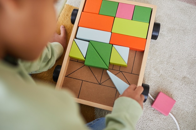 Draufsicht, Nahaufnahme eines nicht erkennbaren afroamerikanischen Kindes, das mit Holzspielzeug spielt, während es zu Hause auf dem Boden sitzt, Kopierraum