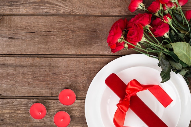 Draufsicht Nahaufnahme eines romantischen Abendessens mit einem Strauß roter Rosen und Geschenk über dem weißen Teller. Stillleben