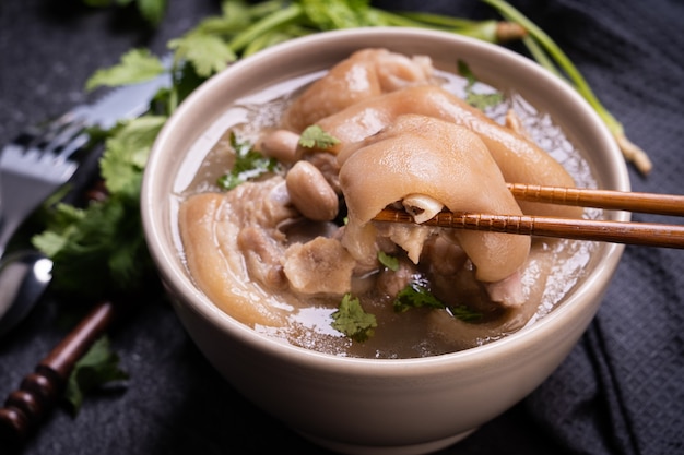 Draufsicht, nahaufnahme, kopierraum, taiwanesisches asiatisches unverwechselbares straßenessen, erdnussschweinefleischknöchelsuppe in einer beige-elfenbeinfarbenen cremeweißen schüssel, die auf dunklem schieferschiefertisch lokalisiert wird