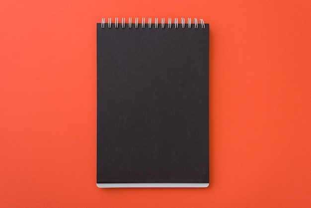 Draufsicht offenen gewundenen leeren schwarzen Notizbuches L auf orange Schreibtischhintergrund, Platz für Ihren Text