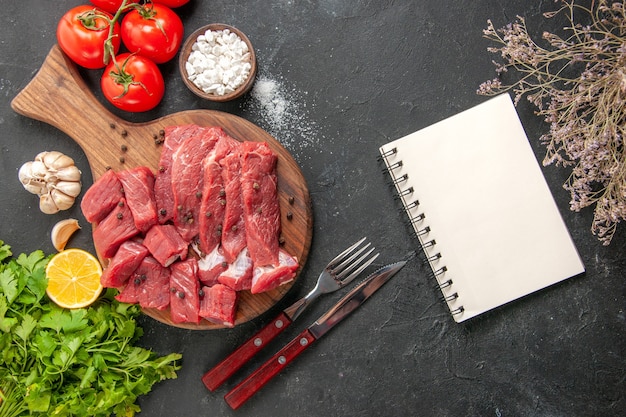 Draufsicht rohe Fleischscheiben mit roten Tomaten und Grüns auf dunkelgrauem Tisch