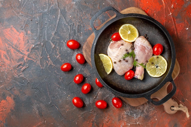 Draufsicht rohes Huhn mit Zitrone und Kirschtomaten in der Pfanne auf dunklem Hintergrund Gericht Mahlzeit Küche Lebensmittelfarbe Gemüsefleisch