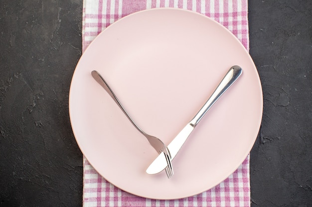 Draufsicht rosa Platte mit Gabel und Messer auf dunklem Hintergrund