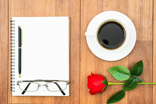 Draufsicht Rote Rosen und Kaffeetasse auf Holztisch und Stift auf Notizblock auf Holzdeck