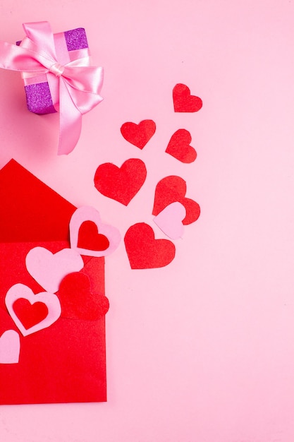 Draufsicht rotes Herz Aufkleber roter Umschlag Geschenk auf rosa Hintergrund