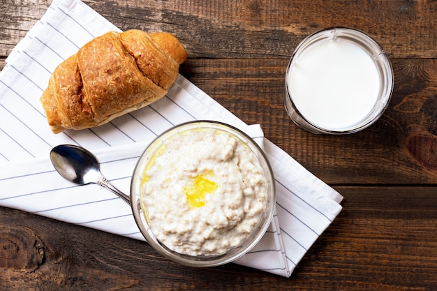 Draufsicht rustikales Frühstück mit Haferbrei, Glas Milch und Croissant auf Braun