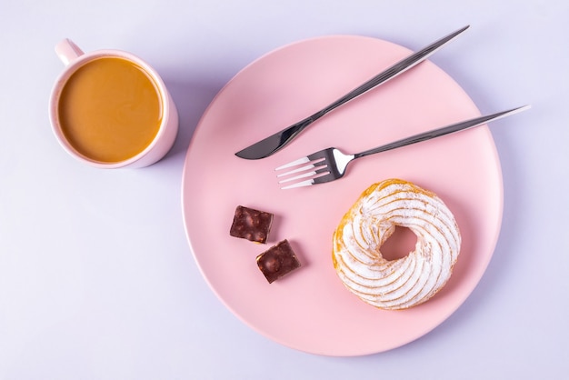 Draufsicht stillleben des kuchens auf einem rosa teller, besteck und tassen mit kakao oder kaffee mit milch. selektiver fokus, horizontale ausrichtung.