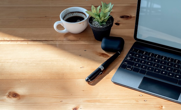 Draufsicht-Tabletttastatur, Tasse Kaffee, Stift und Zimmerpflanze auf hölzernem Tisch mit Kopierraum