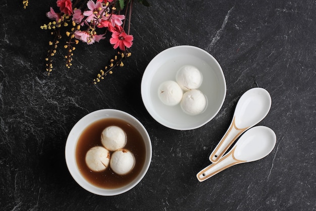 Draufsicht Tang Yuan (Wedang Ronde), chinesische Klebreis-Knödelbällchen mit Zucker-Ingwer oder Palmzuckersirup auf rotem Chinesen auf schwarzem Hintergrund für Wintersonnenwende-Neujahrsfest-Essen.