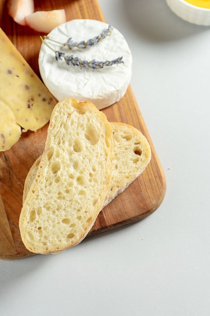 Draufsicht verschiedene Arten von Käse auf Holzschneidebrett. Käse mit Feigenpfirsich, Honig, Ciabatta und Nüssen, Glas Rotwein. Stilvolle Lebensmittelwohnung lag auf grauem Hintergrund. Speicherplatz kopieren. Weicher Fokus