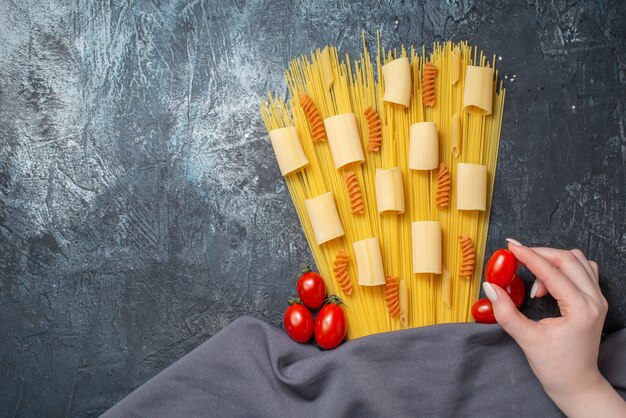 Draufsicht verschiedene Pasta Rigatoni Spaghetti Spiralen Kirschtomate in weiblicher Hand lila Schal auf grauem Hintergrund Freiraum