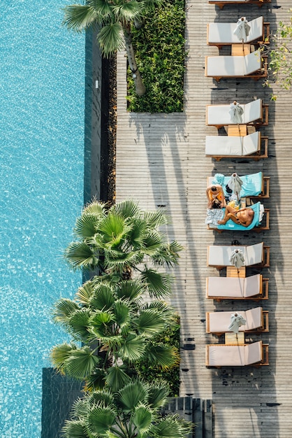 Draufsicht von den Touristen, die auf Stühlen im Freien sitzen, nähern sich Swimmingpool mit Palmen in der Hotelanlage.