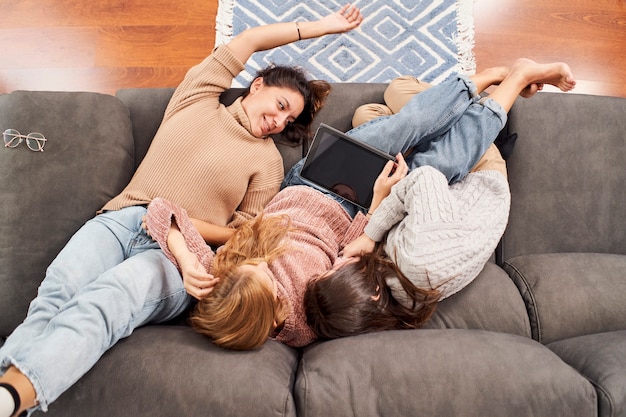 Draufsicht von drei Freundinnen auf der Couch zu Hause, die eine Tablette betrachten