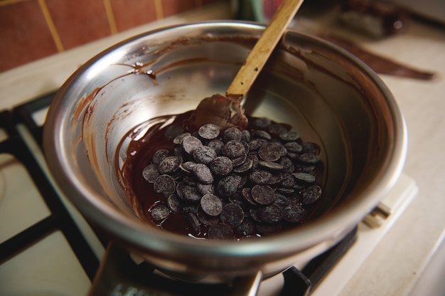 Draufsicht von dunklen Schokoladentabletten in einer Schüssel auf Wasserbad. Herstellung von hausgemachten Pralinen zur Feier des Weltschokoladentages