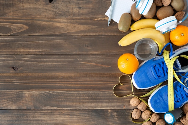 Draufsicht von einigen natürlichen Nahrungsmitteln, Turnschuhen und Maßband auf einem dunklen Holztischhintergrund. Konzept von Gesundheit, Ernährung und Sport.