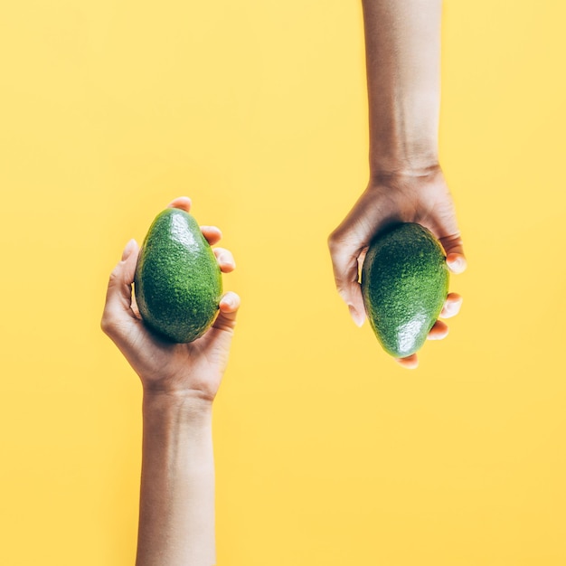 Draufsicht von Frauenhänden, die Avocado auf gelbem Hintergrund halten
