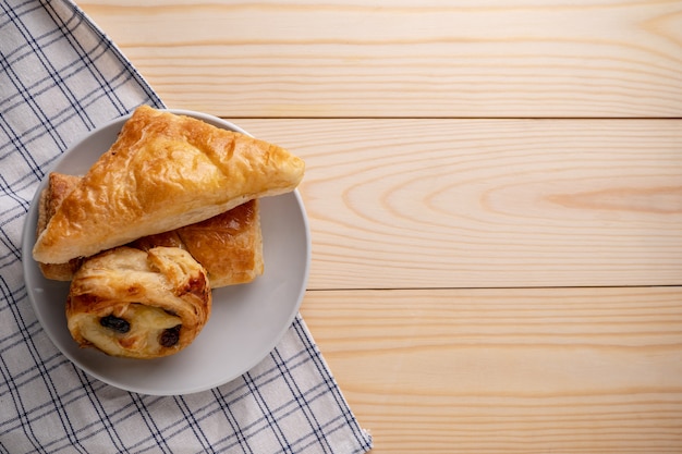 Draufsicht von frischen süßen Brötchen und von Torte gesetzt auf einen hölzernen Behälter und eine Serviette zum Morgenfrühstück.