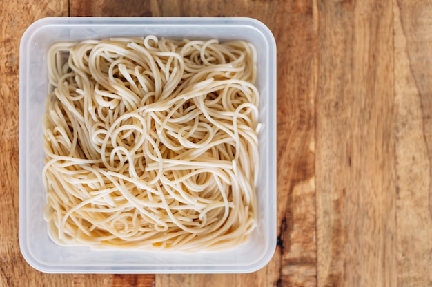 Draufsicht von gekochten Spaghetti-Nudeln in Plastikbox auf Holztisch