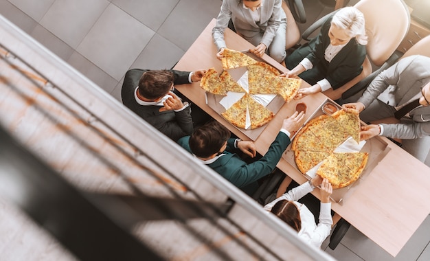 Draufsicht von Geschäftsleuten in der formellen Kleidung, die Pizza zusammen am Arbeitsplatz essen. Erfolg bei der Arbeit beginnt mit einer positiven Einstellung.