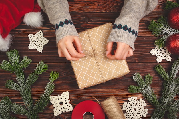 Draufsicht von Händen einer Frau mit einem Weihnachtsgeschenk auf hölzernem Hintergrund