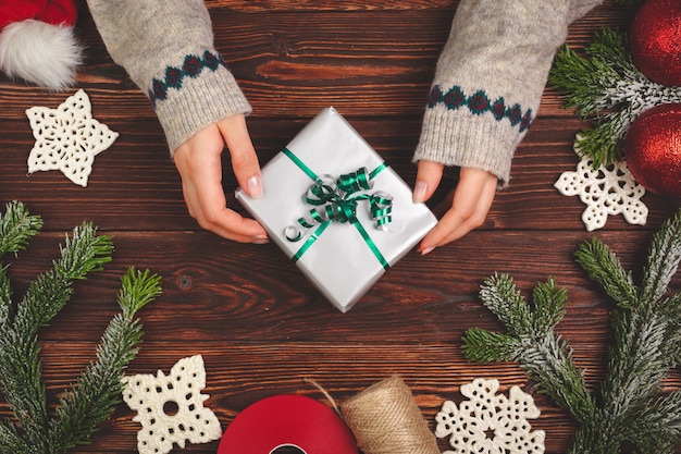 Draufsicht von Händen einer Frau mit einem Weihnachtsgeschenk auf hölzernem