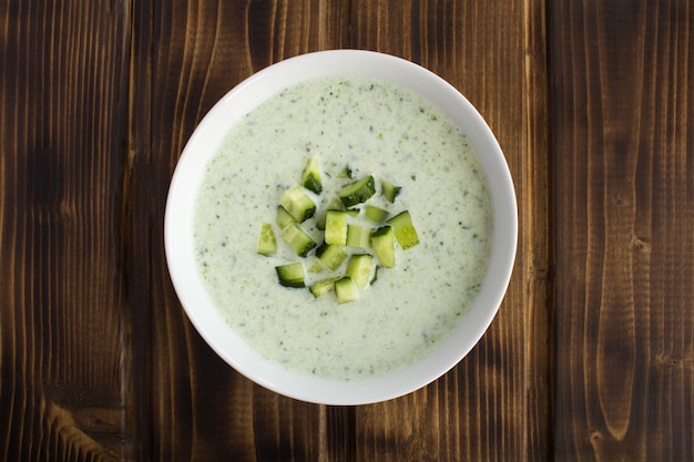 Draufsicht von Joghurt-Smoothies mit Gurke in der weißen Schüssel auf dem Holz