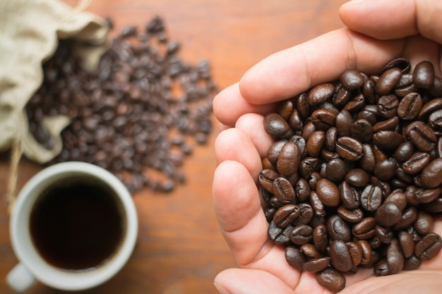 Draufsicht von Kaffeebohnen an Hand und Kaffeebohnen und Kaffeetasse auf Holztisch.