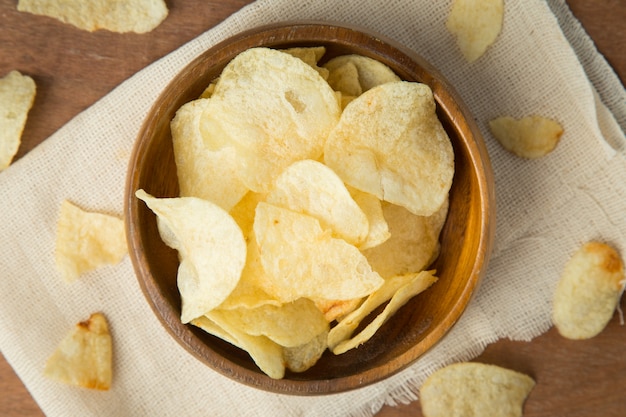 Draufsicht von Kartoffelchips in der hölzernen Schüssel, die auf Leinen und hölzernen Hintergrund sich setzt.