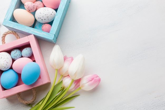 Draufsicht von niedlichen kisten mit bunten ostereiern und tulpen