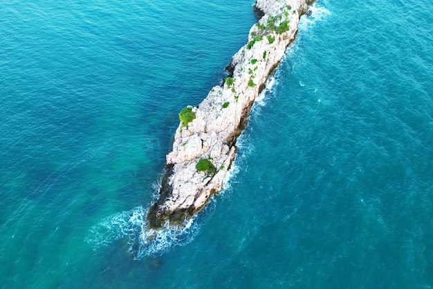 Draufsicht von oben von einer Drohne auf eine einsame, schöne Insel im Meer mit Wellen. Schöne felsige Insel über blauem Himmel