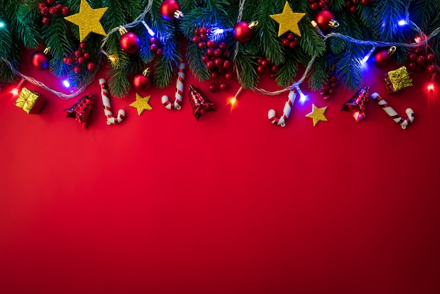 Draufsicht von Weihnachtsfichtenzweigen, von Kiefernkegeln, von roten Beeren und von Glocke auf rotem Hintergrund.