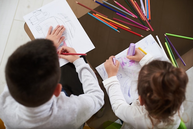 Draufsicht von zwei niedlichen Kindern, die mit Farbstiften zu Hause zeichnen
