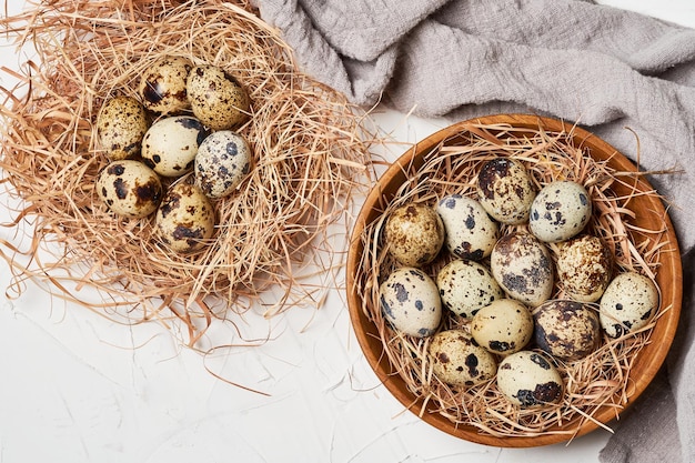 Draufsicht Wachteleier in Holzschale und Nest auf weißem Tischhintergrund