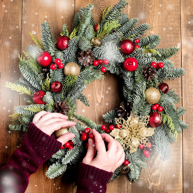 Draufsicht Weibliche Hände Florist Hand machen Weihnachtskranz auf Holztisch Holzhintergrund Schnee