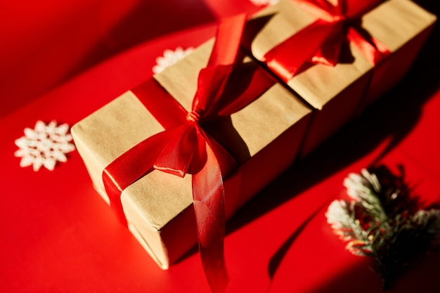 Draufsicht Weihnachten umweltfreundliche Verpackung aus Kraftpapier und Tannenzweigen Geschenke für die Weihnachtszeit auf rotem Hintergrund, hartes Licht