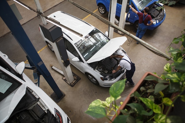 Draufsichtaufnahme eines professionellen Automechanikers, der in der Werkstatt unter der Motorhaube eines Autos arbeitet