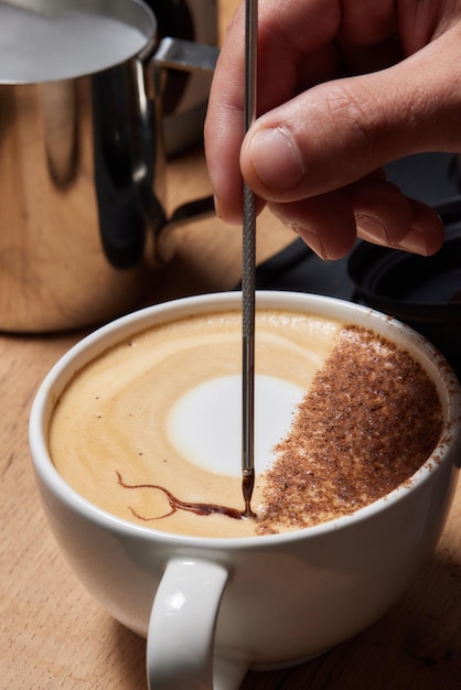 Draufsichtaufnahme eines professionellen Baristas, der Milch aus einem Glas in eine Tasse Kaffee gießt Kaffee wird vorbereitet