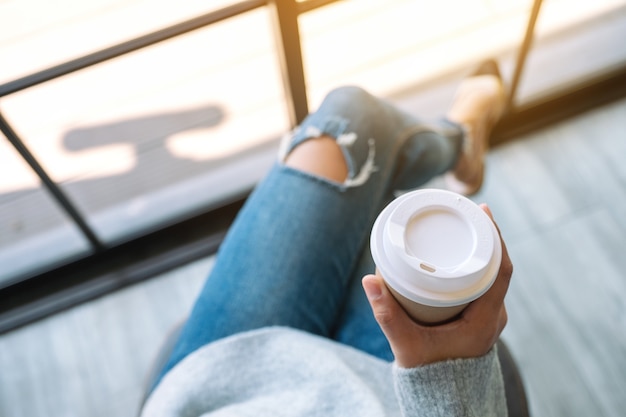 Draufsichtbild einer frau, die morgens eine papiertasse heißen kaffees sitzt und hält