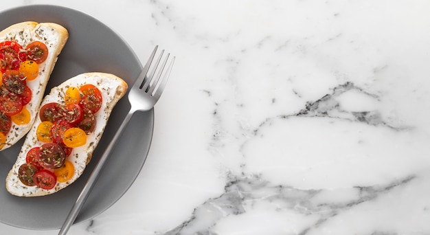 Draufsichtbrot mit Frischkäse und Kirschtomaten auf Teller mit Gabel und Kopierraum