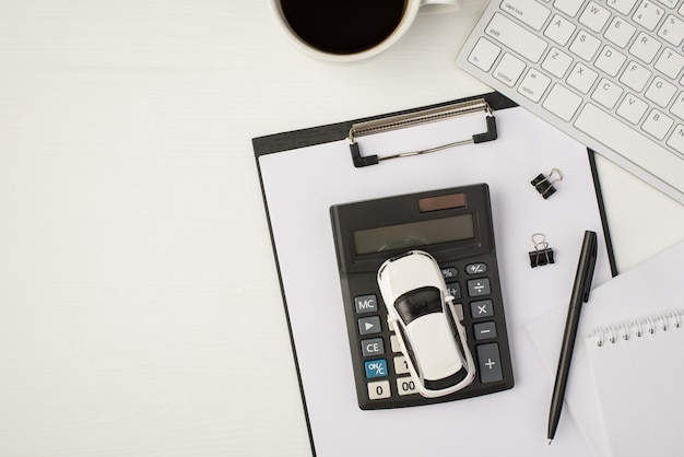 Draufsichtfoto des Geschäftsarbeitsplatzes mit Tastatur, Notizbuch, Stift, Tasse Kaffee, Papierordner und Automodell auf Taschenrechner auf isoliertem weißem Hintergrund mit Copyspace