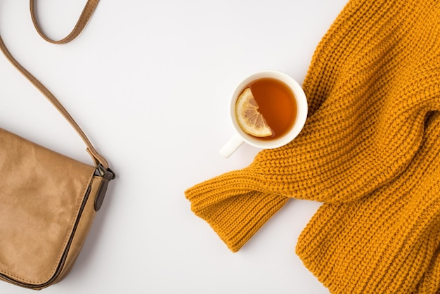 Draufsichtfoto einer orangefarbenen Pullovertasse Tee mit Zitrone und Lederhandtasche auf isoliertem weißem Hintergrund