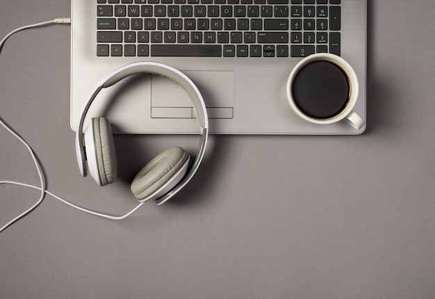 Draufsichtfoto von kabelgebundenen weißen Kopfhörern und einer Tasse Kaffee auf der Laptoptastatur auf isoliertem grauem Hintergrund
