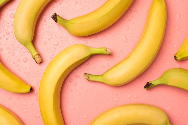 Draufsichtfoto von reifen gelben Bananen und Wassertropfen auf isoliertem pastellrosa Hintergrund