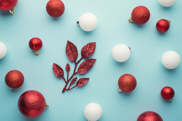 Draufsichtfoto von weißen und roten Christbaumschmuckkugeln und Zweigen auf isoliertem pastellblauem Hintergrund