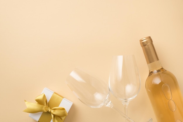 Draufsichtfoto von zwei Weingläsern, Flasche Weißwein und weißer Geschenkbox mit goldener Schleife auf isoliertem beigem Hintergrund mit Copyspace