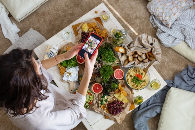 Draufsichtfrau, die Esstisch mit dem Servieren von leckerem Essen und Trinken fotografiert, verwendet Smartphone