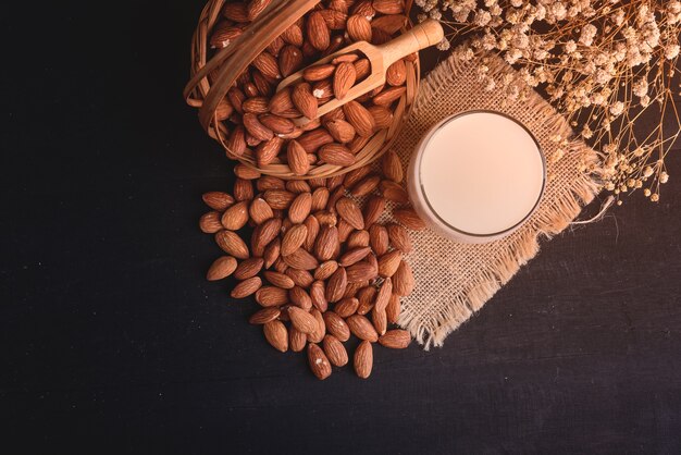 Draufsichtglas Milch mit hölzernem Löffel und Mandeln auf schwarzem Holztischhintergrund.